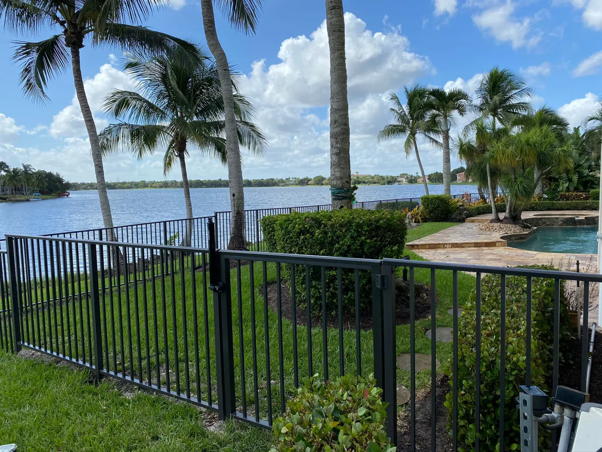 Black fence bordering a waterfront lawn beneath South Florida palms