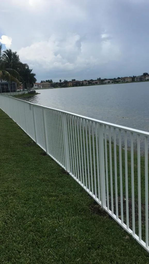 White aluminum fence running along a lakefront lawn