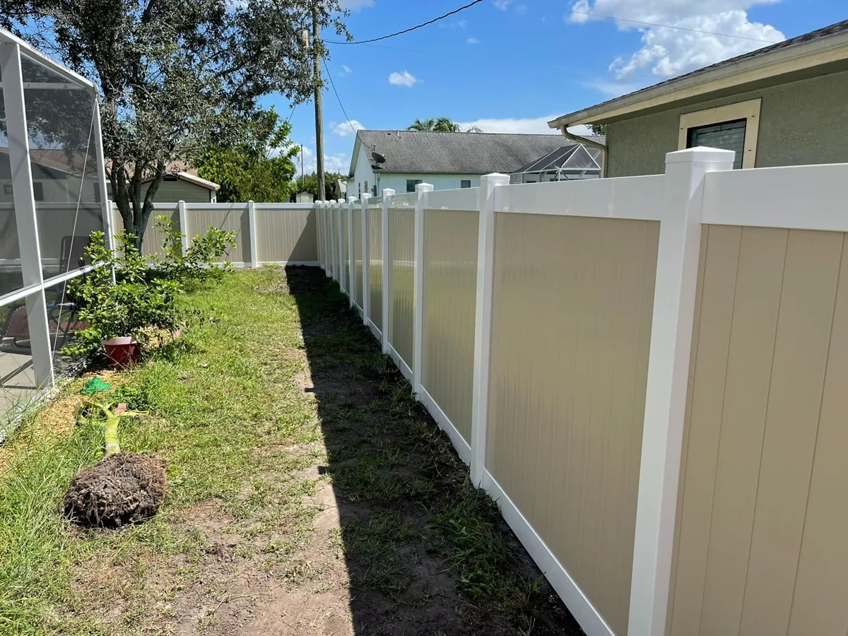 Tan vinyl privacy fence with white posts along a narrow side yard