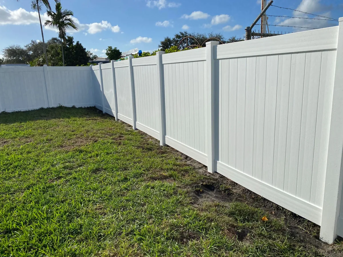 White vinyl privacy fence with matching posts along a backyard lawn