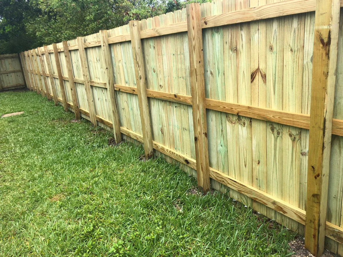 Vertical wood fence with visible horizontal rails along a lawn